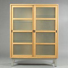 Ditlev Karsten Vitrine af massiv eg med ben og greb af stål, front med skydelåger, bag hvilke hylder. Udført hos Brdr. Andersen. H. 159. B. 122. D. 43.
